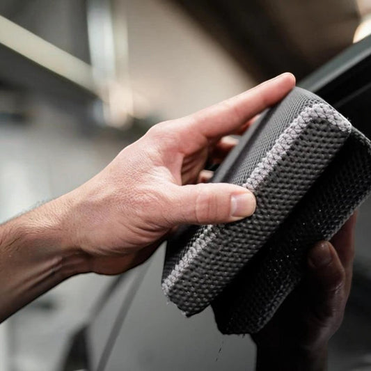 T-Top Vibes AllGuard 2-in-1 clay scrubber and bug removal pad being held against a car window for detailing