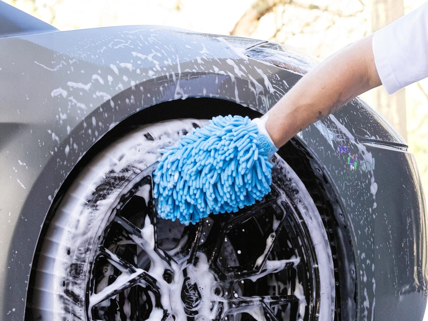T-Top Vibes blue chenille microfiber car wash mitt cleaning a soapy black car wheel with an elastic wrist cuff