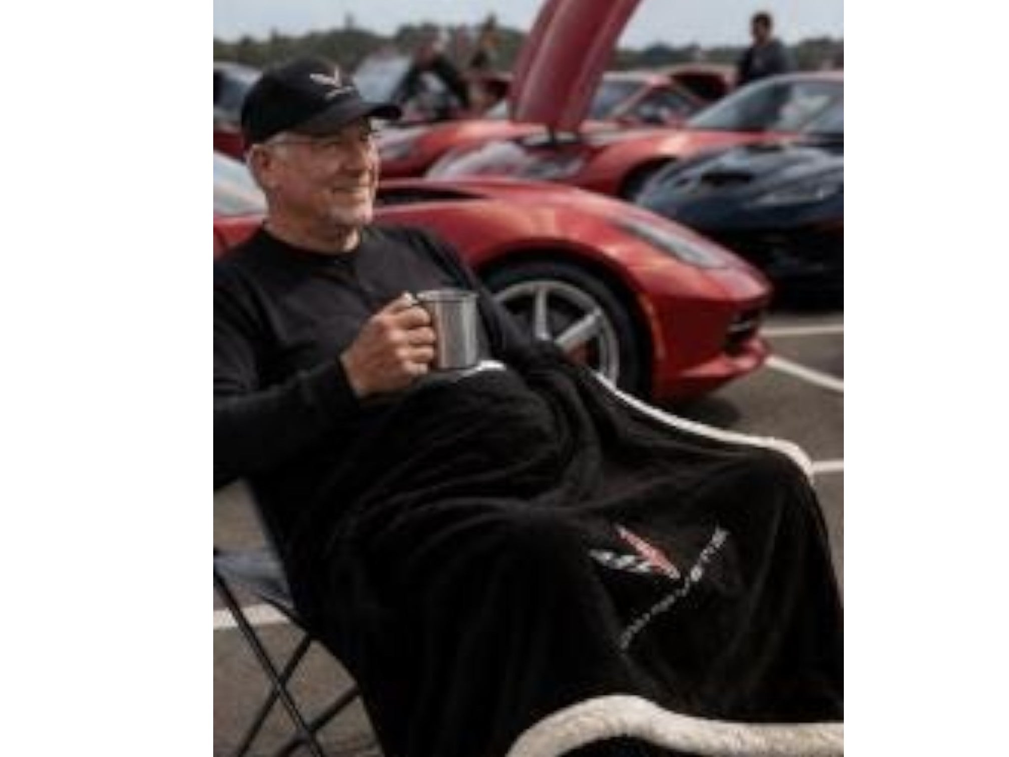 T-Top Vibes black Corvette plush sherpa throw blanket with embroidered logo, used by a man at a car show.