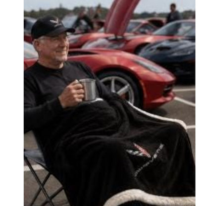 T-Top Vibes black Corvette plush sherpa throw blanket with embroidered logo, used by a man at a car show.